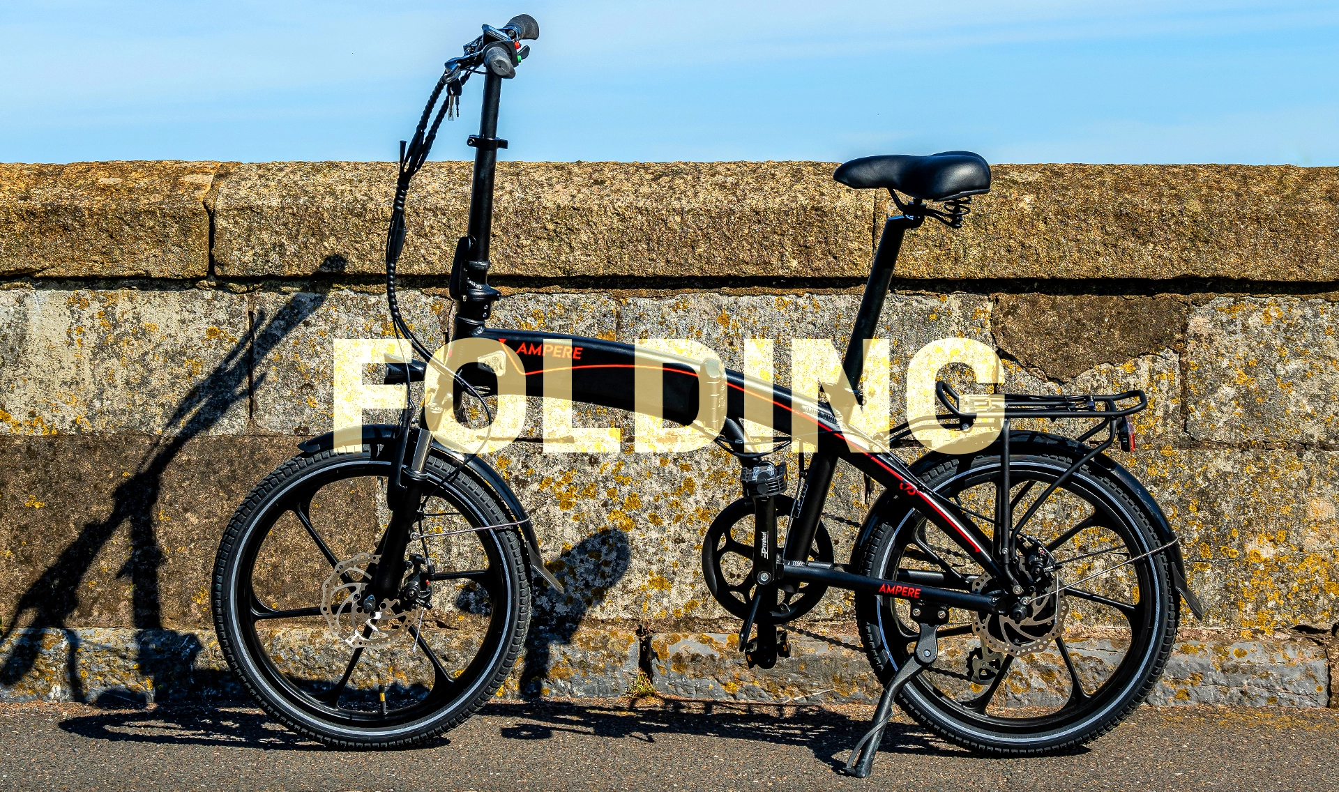 A black and red Ampere Electric folding bike in front of a low wall