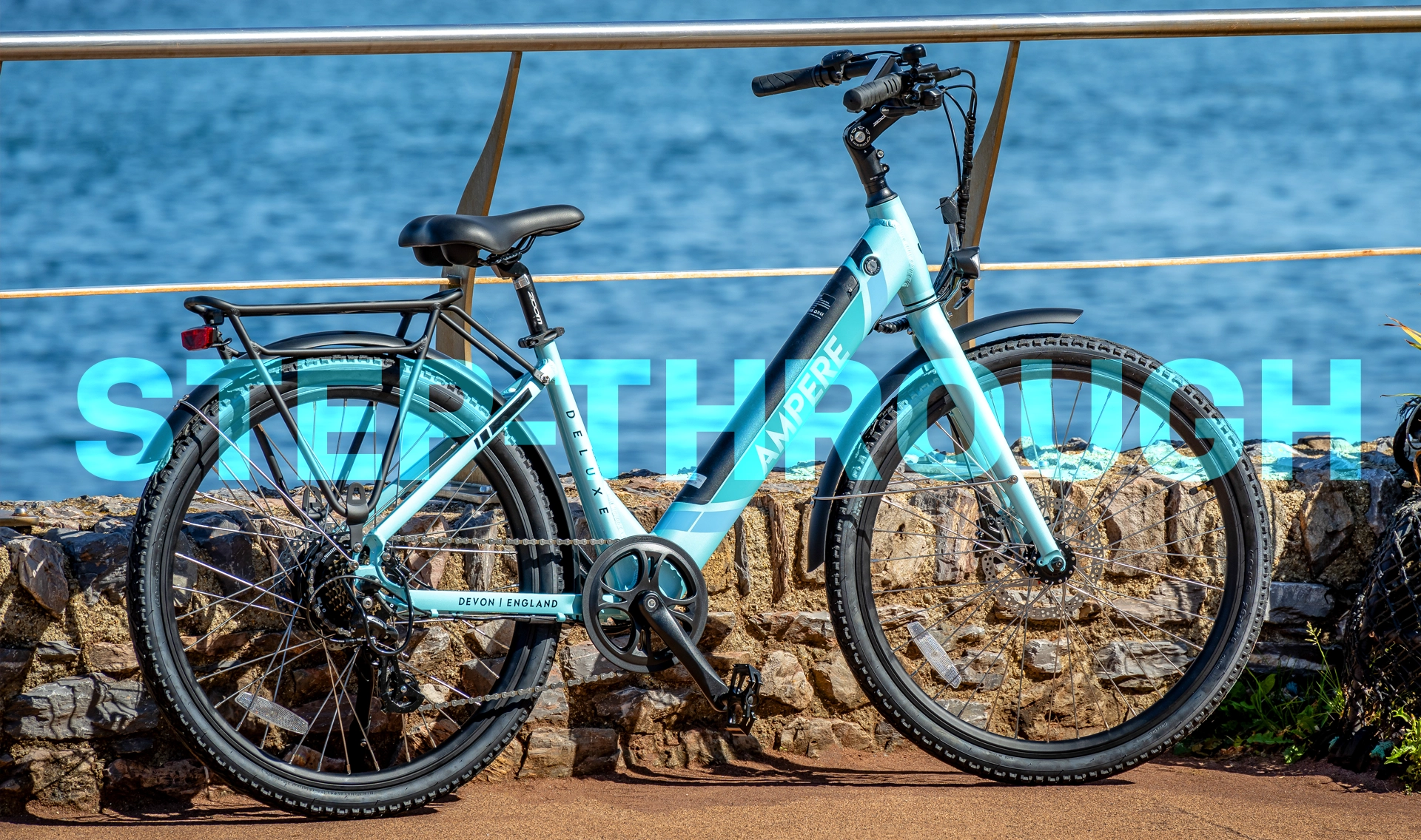 A black and blue Ampere Electric step-through bike in front of a low wall showing the ocean